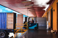 Forklift stuffing-unstuffing pallets of cargo to container on warehouse leveler dock.